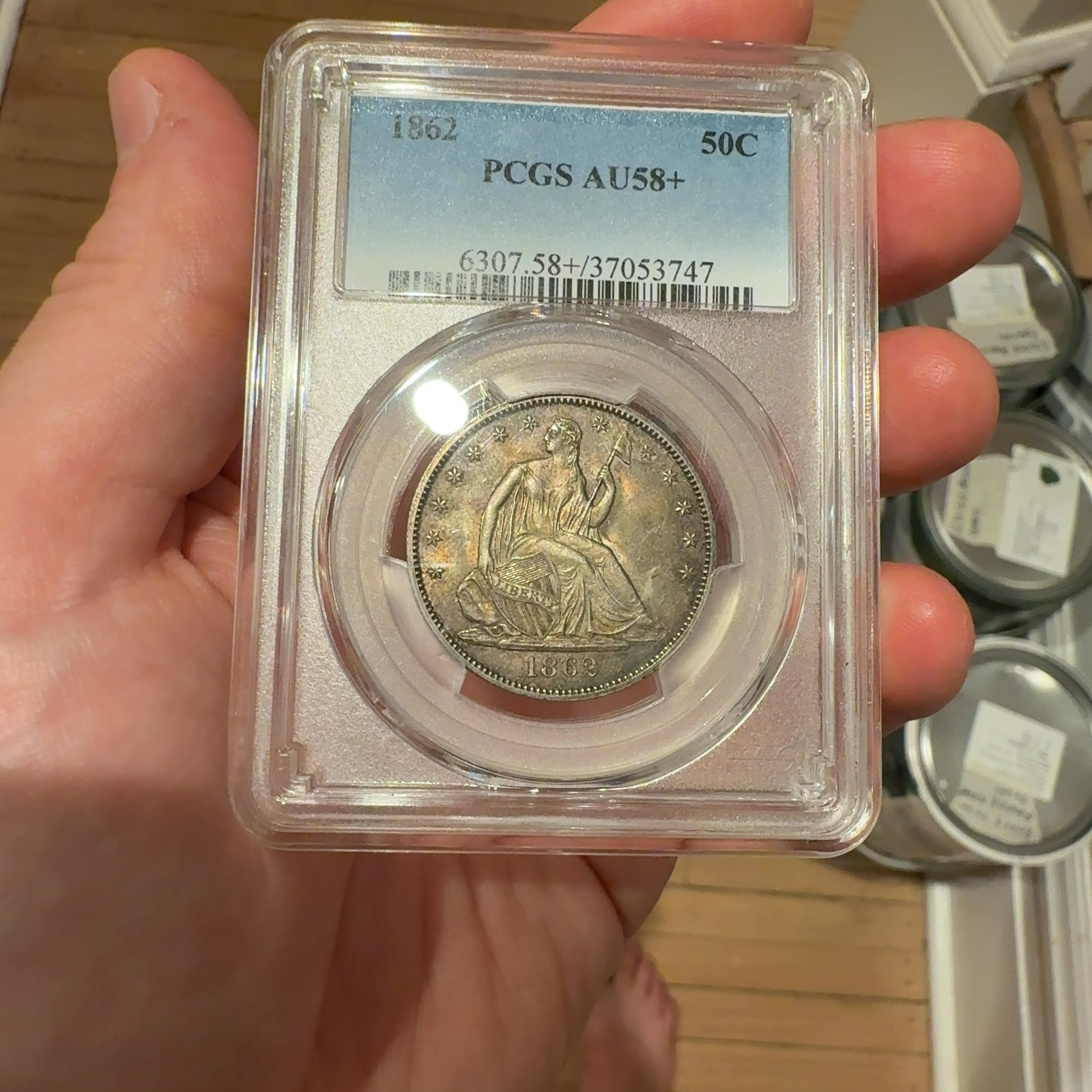 Handheld phone photograph 1 of the 1862 Seated Liberty Half Dollar in its holder
