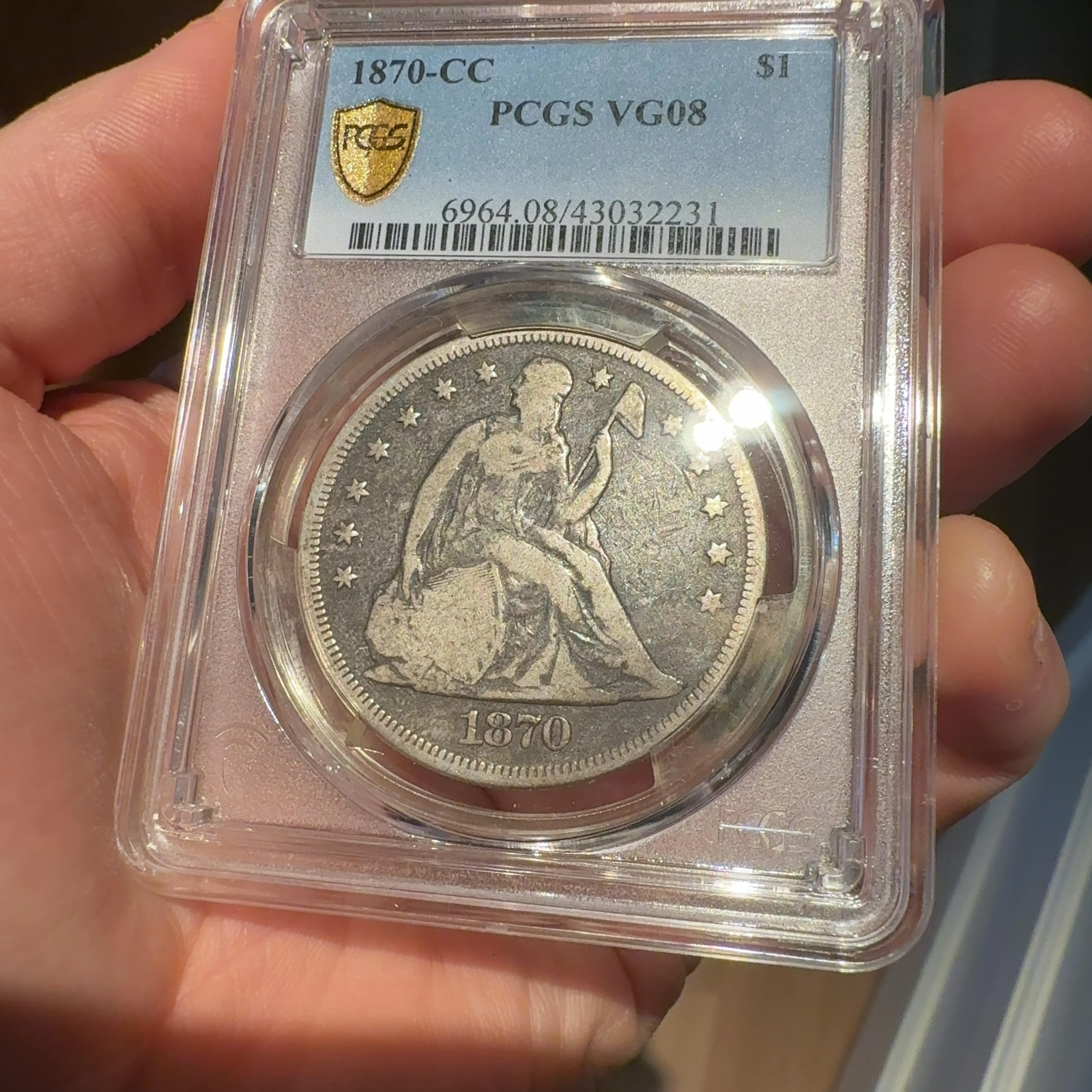 Handheld phone photograph 3 of the 1870-CC Seated Liberty Dollar in its holder