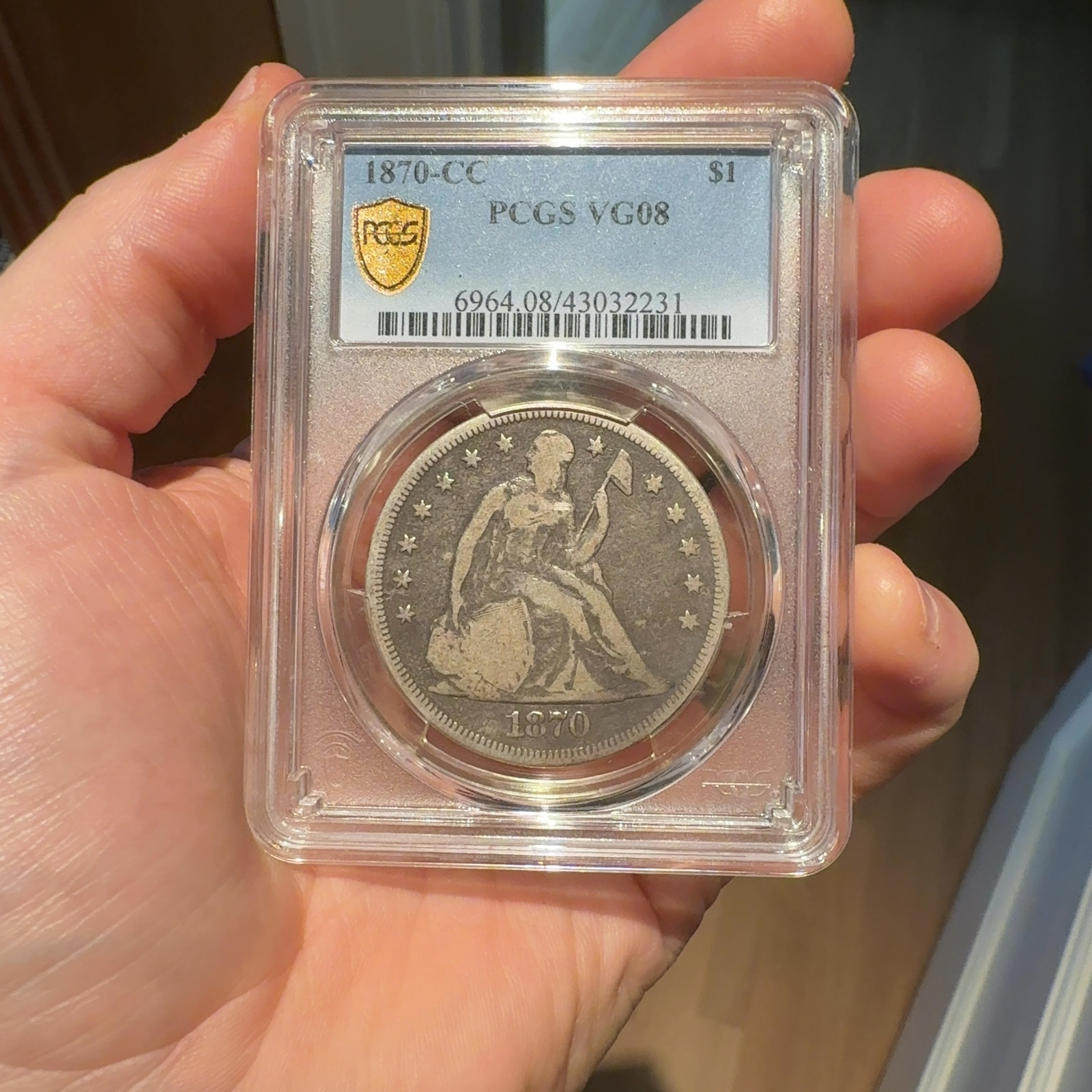 Handheld phone photograph 1 of the 1870-CC Seated Liberty Dollar in its holder
