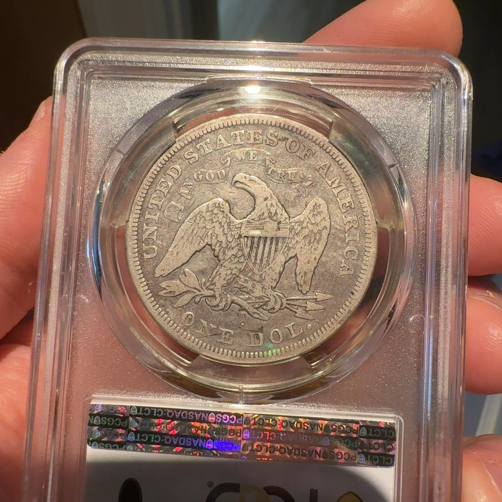 Handheld phone photograph 8 of the 1870-CC Seated Liberty Dollar in its holder