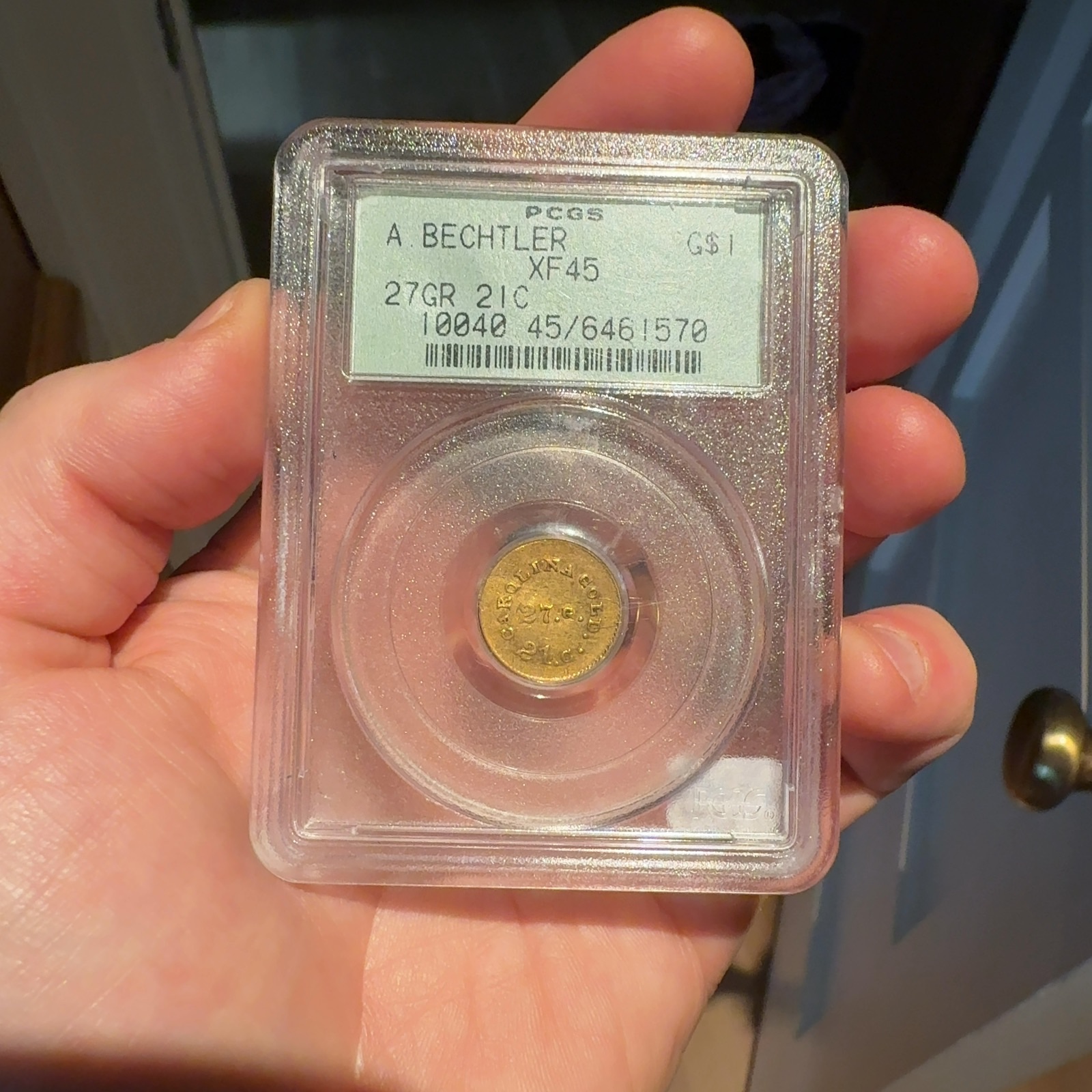 Handheld phone photograph 1 of the 1830s Bechtler Gold Dollar in its holder