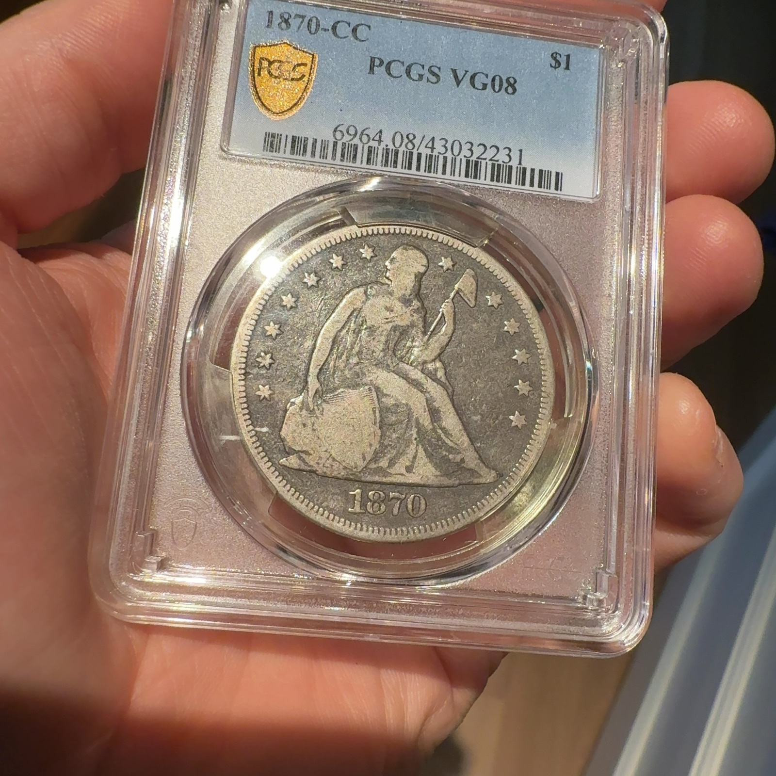 Handheld phone photograph 4 of the 1870-CC Seated Liberty Dollar in its holder
