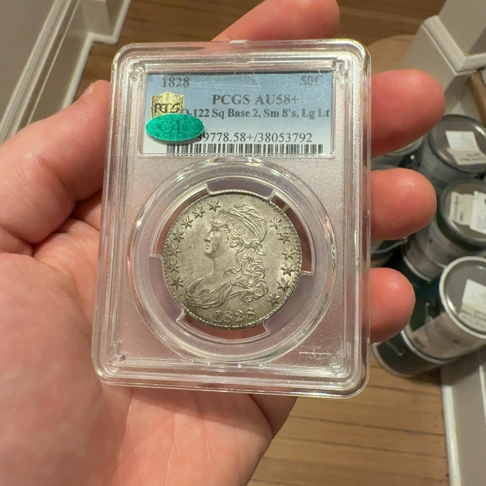 Handheld phone photograph 4 of the 1828 Capped Bust Half Dollar in its holder