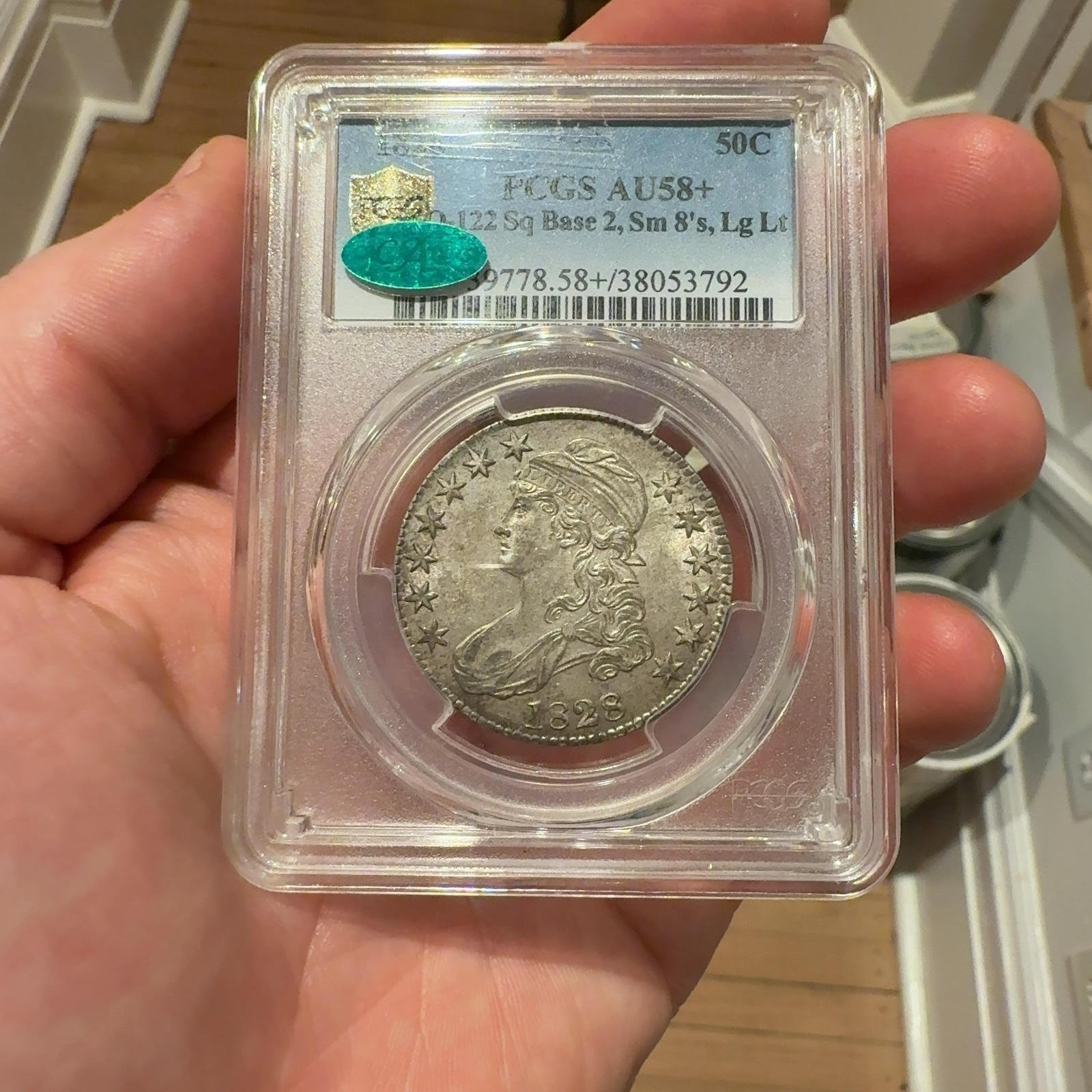 Handheld phone photograph 1 of the 1828 Capped Bust Half Dollar in its holder