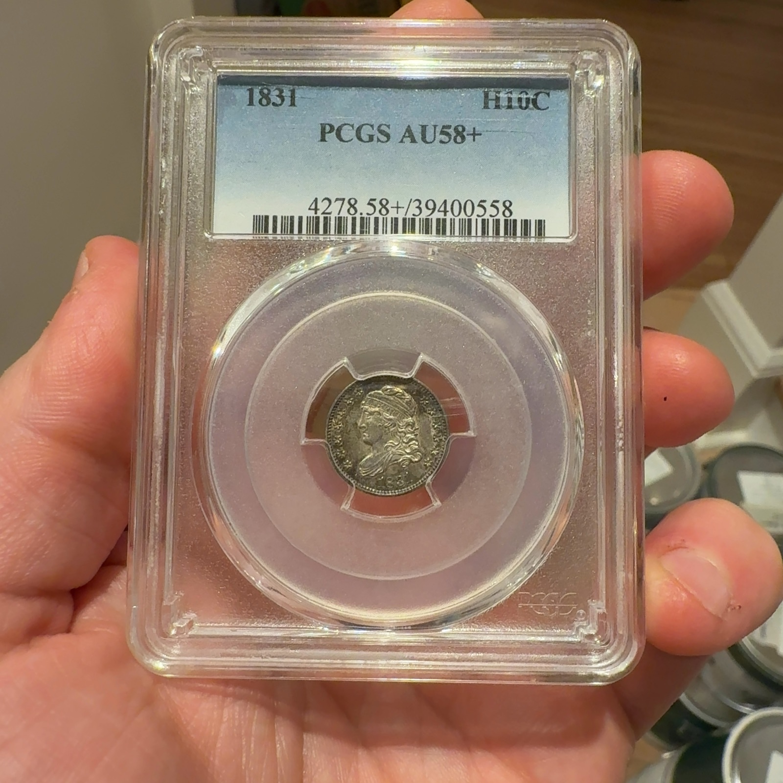 Handheld phone photograph 1 of the 1831 Capped Bust Half Dime in its holder