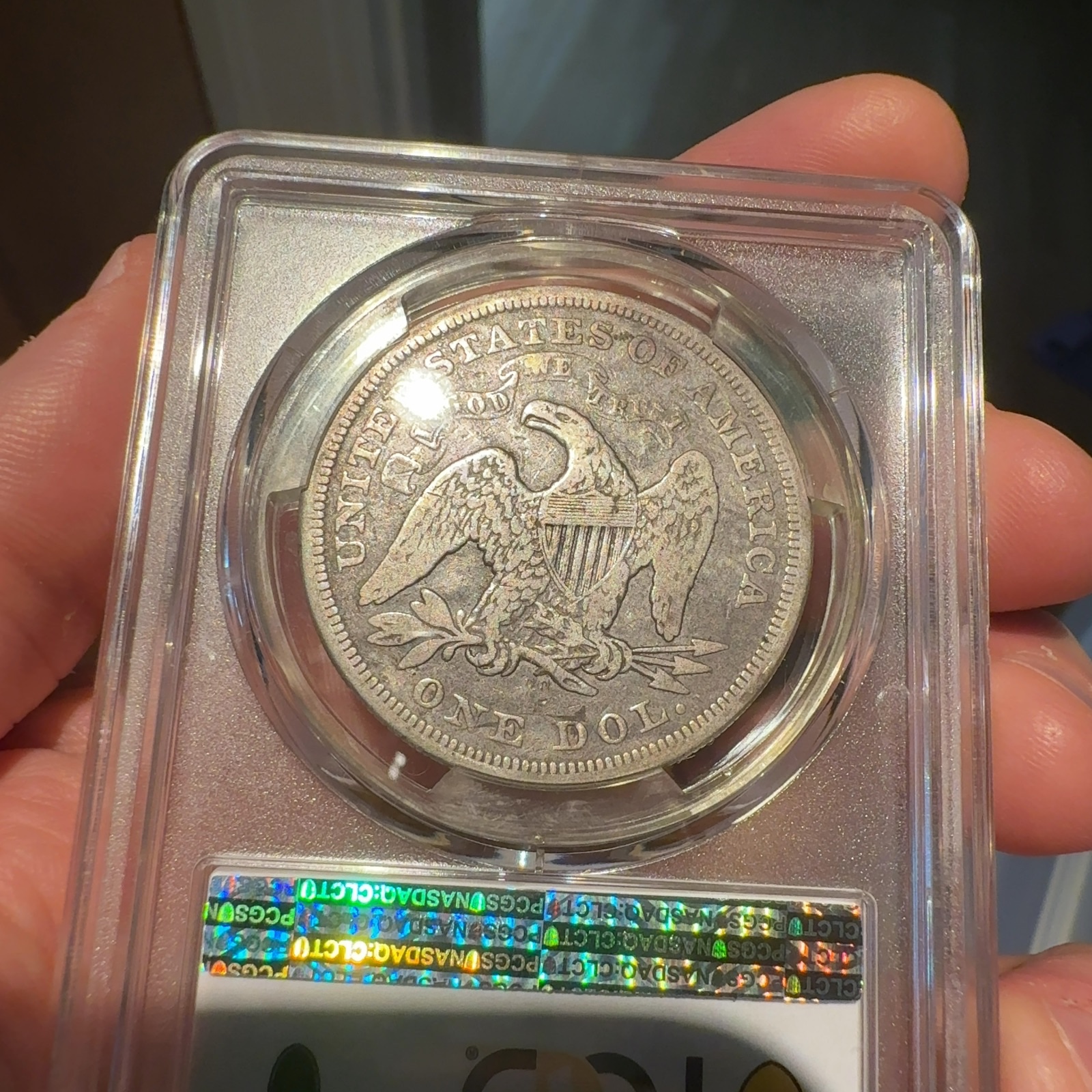 Handheld phone photograph 7 of the 1870-CC Seated Liberty Dollar in its holder