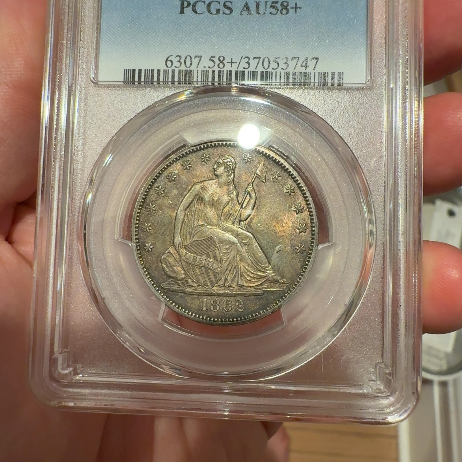 Handheld phone photograph 2 of the 1862 Seated Liberty Half Dollar in its holder
