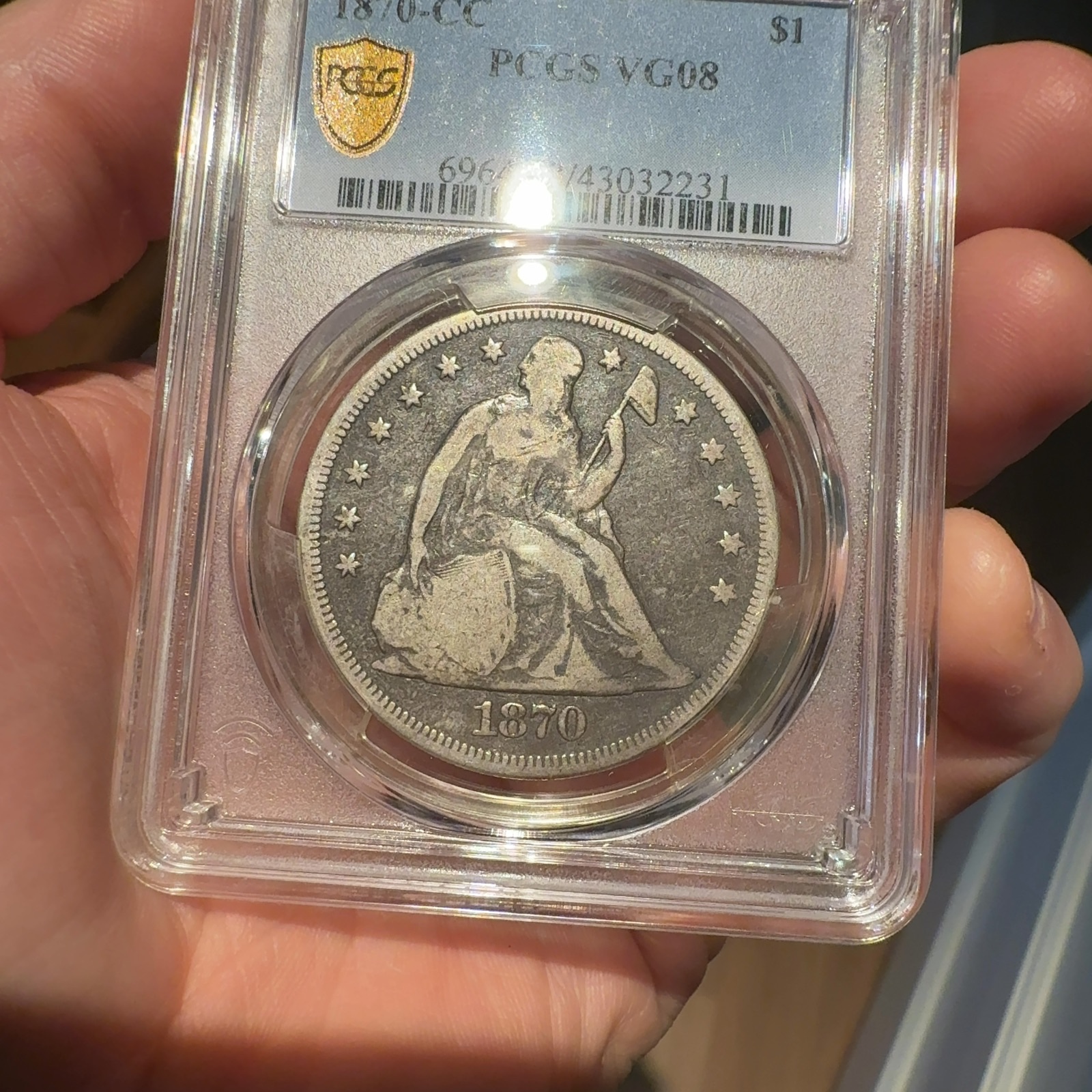 Handheld phone photograph 2 of the 1870-CC Seated Liberty Dollar in its holder