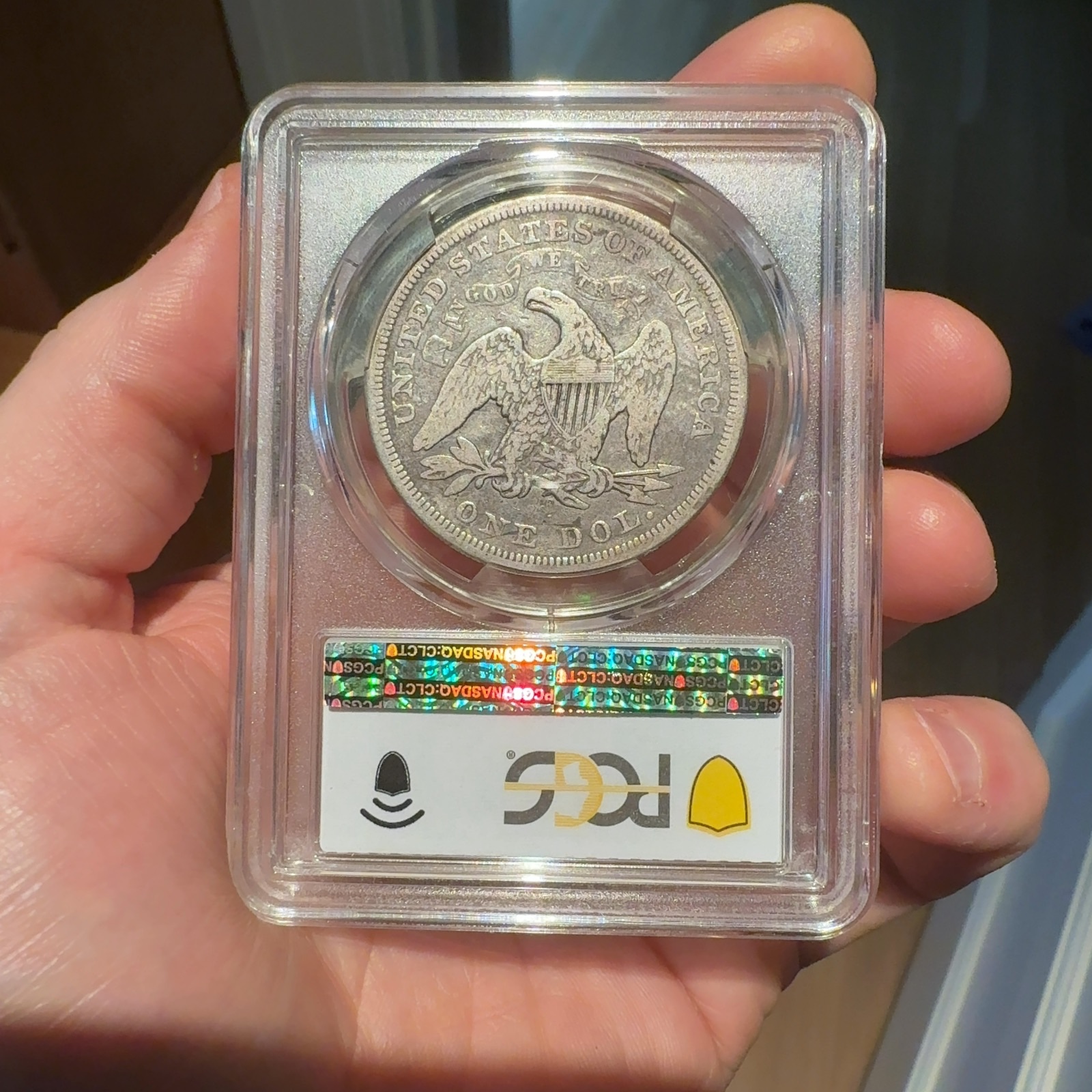 Handheld phone photograph 5 of the 1870-CC Seated Liberty Dollar in its holder