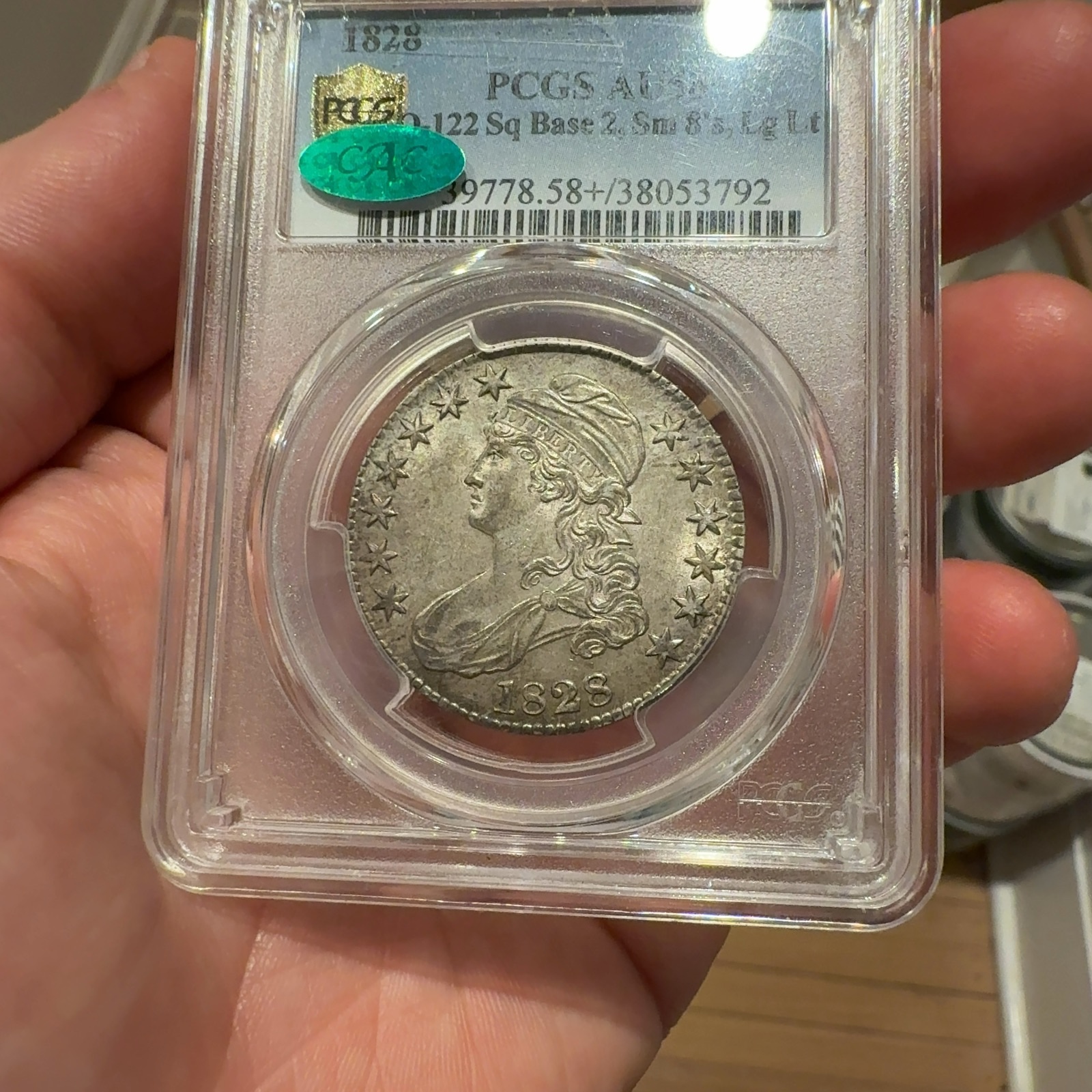 Handheld phone photograph 2 of the 1828 Capped Bust Half Dollar in its holder