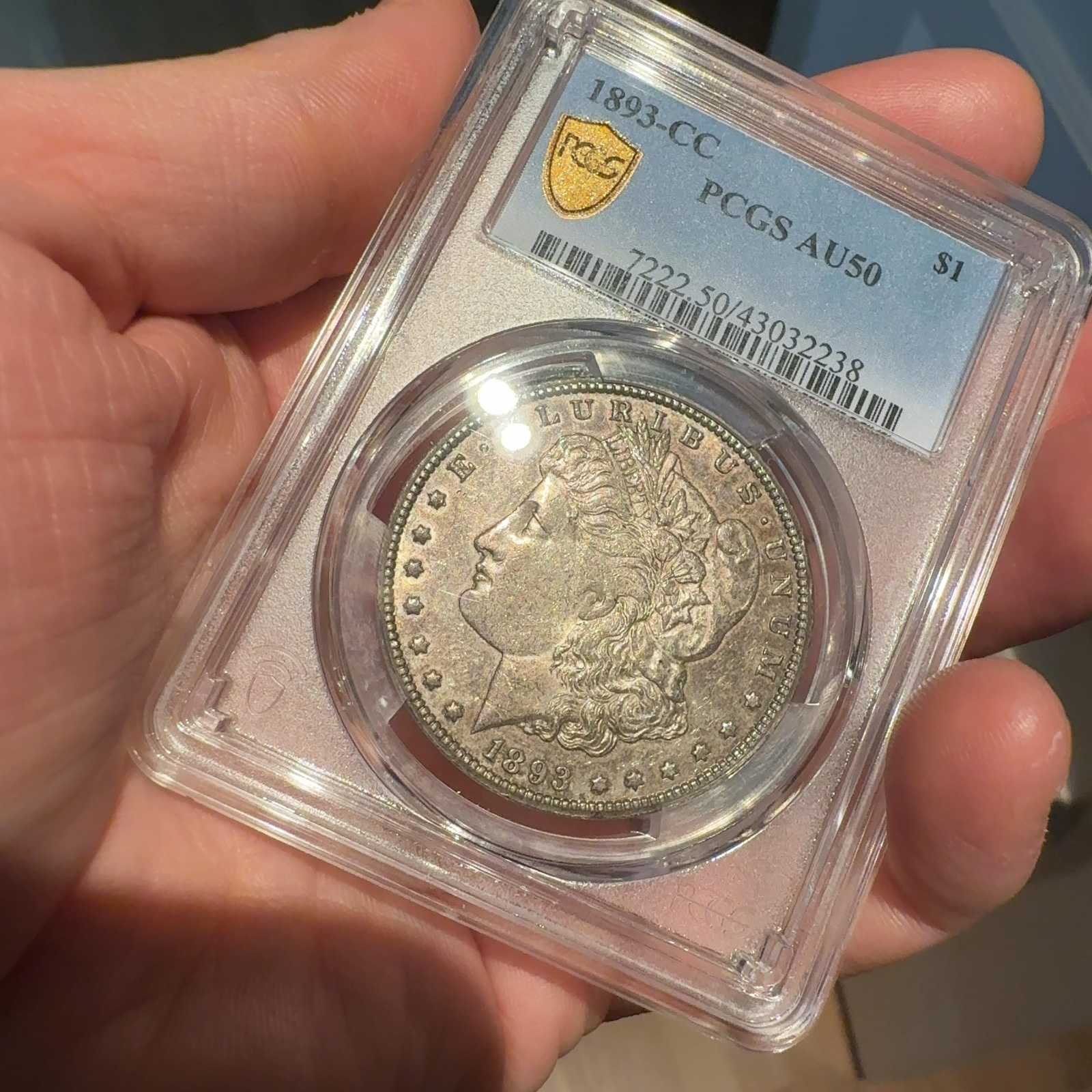 Handheld phone photograph 2 of the 1893-CC Morgan Dollar in its holder