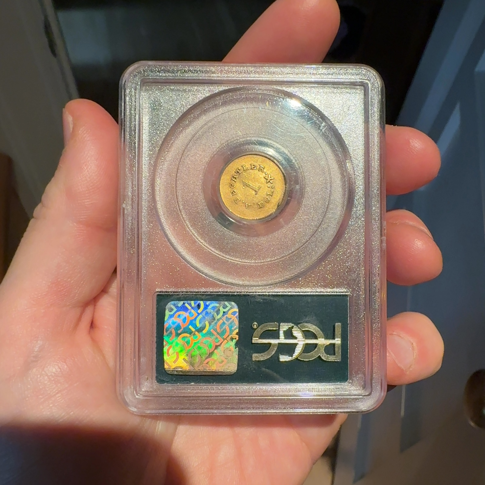 Handheld phone photograph 5 of the 1830s Bechtler Gold Dollar in its holder